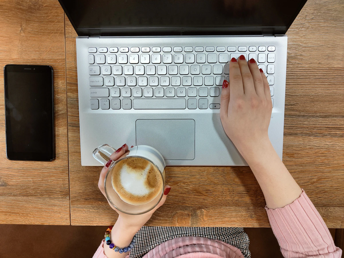 Person typing on a laptop with a cup of coffee nearby