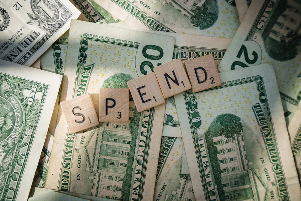 Scrabble tiles spelling SPEND on dollar bills representing recurring expenses