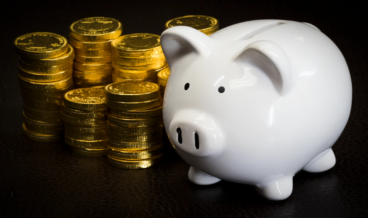 White piggy bank next to stacked gold coins